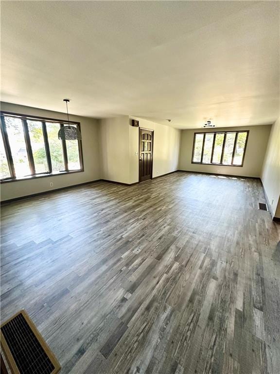 unfurnished living room with dark wood finished floors, visible vents, and a healthy amount of sunlight