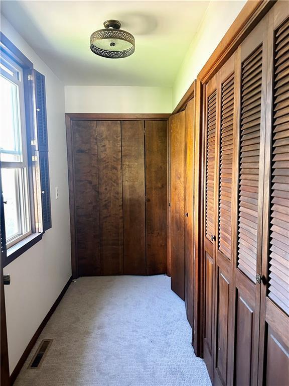 hall featuring light colored carpet, visible vents, and baseboards