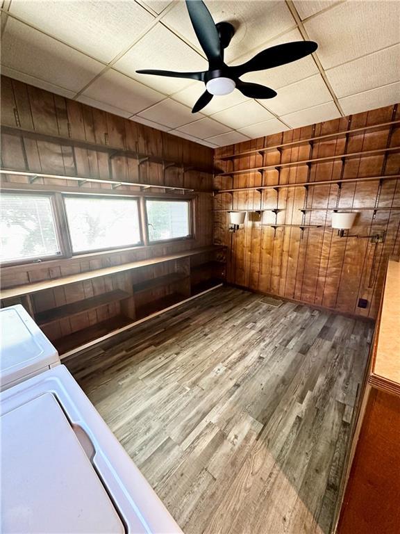 unfurnished room featuring ceiling fan, a paneled ceiling, wood finished floors, and wood walls