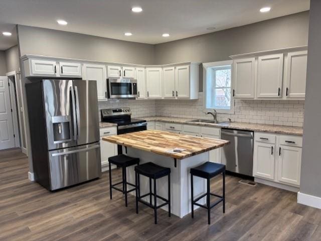 kitchen featuring wooden counters, a kitchen bar, stainless steel appliances, white cabinetry, and a sink