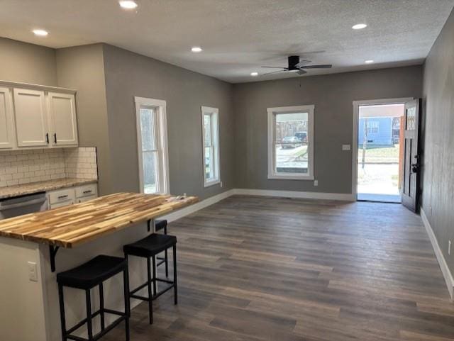 kitchen with baseboards, open floor plan, butcher block counters, white cabinets, and dark wood-style flooring