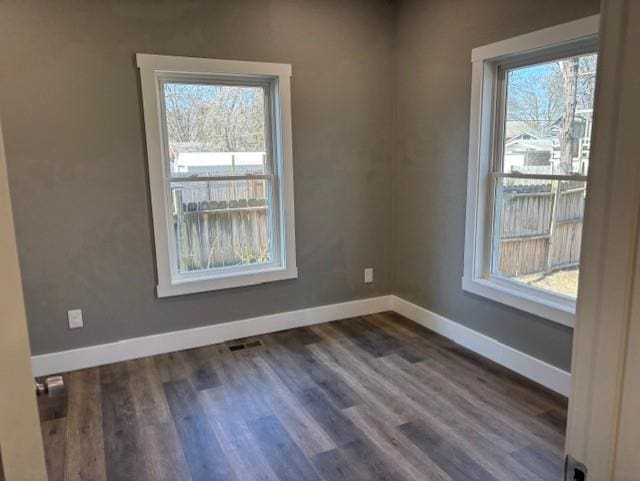 empty room with visible vents, baseboards, a healthy amount of sunlight, and dark wood-style floors