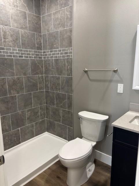 full bath featuring vanity, wood finished floors, baseboards, a stall shower, and toilet