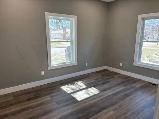 empty room with visible vents, baseboards, and dark wood-style flooring