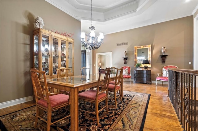 dining space with visible vents, a chandelier, ornamental molding, light wood-style flooring, and a raised ceiling