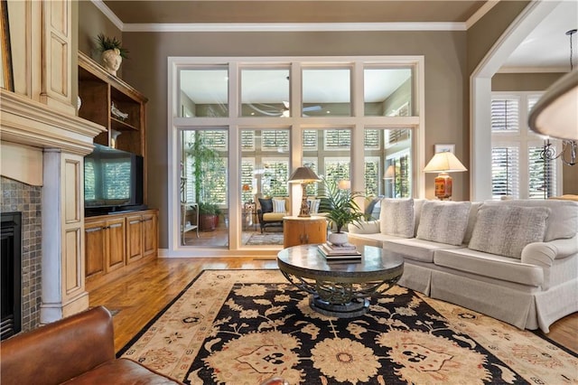 living room featuring a fireplace, a ceiling fan, light wood-style flooring, and crown molding