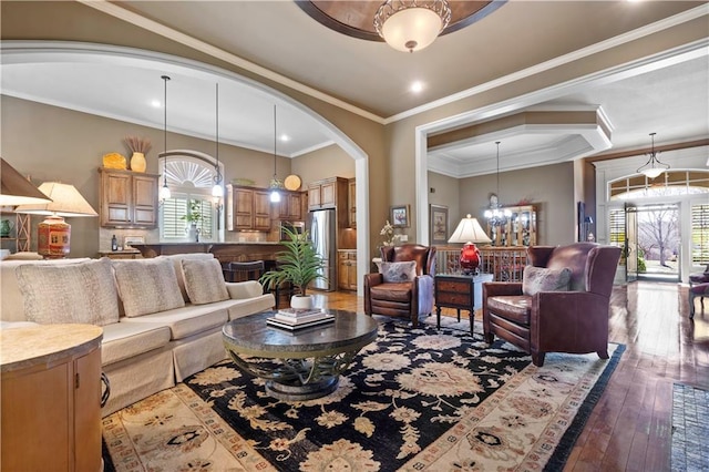 living room featuring arched walkways, a chandelier, ornamental molding, and hardwood / wood-style flooring