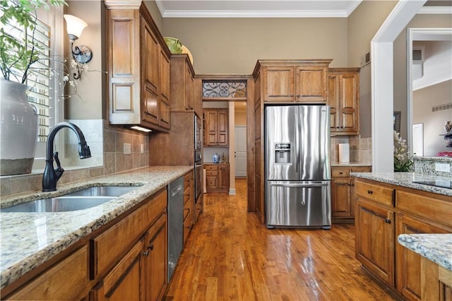 kitchen featuring light wood-type flooring, brown cabinets, ornamental molding, a sink, and appliances with stainless steel finishes