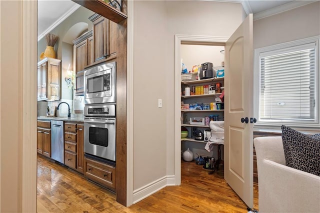 kitchen with ornamental molding, a sink, wood finished floors, stainless steel appliances, and brown cabinetry