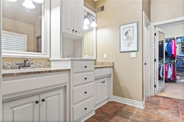 bathroom with double vanity, visible vents, baseboards, and a walk in closet