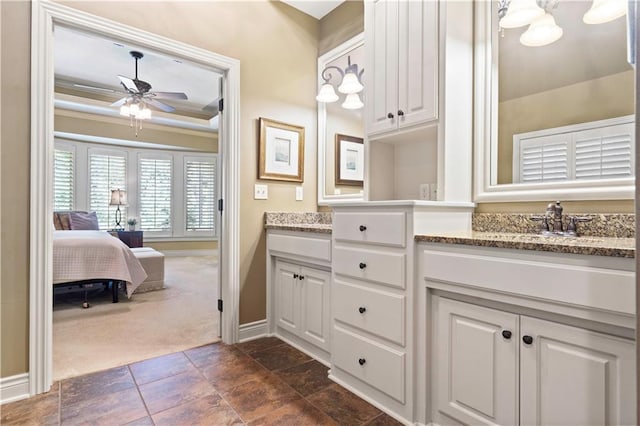 full bathroom featuring baseboards, a tray ceiling, double vanity, a ceiling fan, and a sink