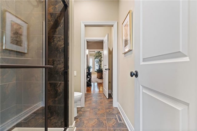 bathroom with a shower stall, toilet, baseboards, and stone finish flooring