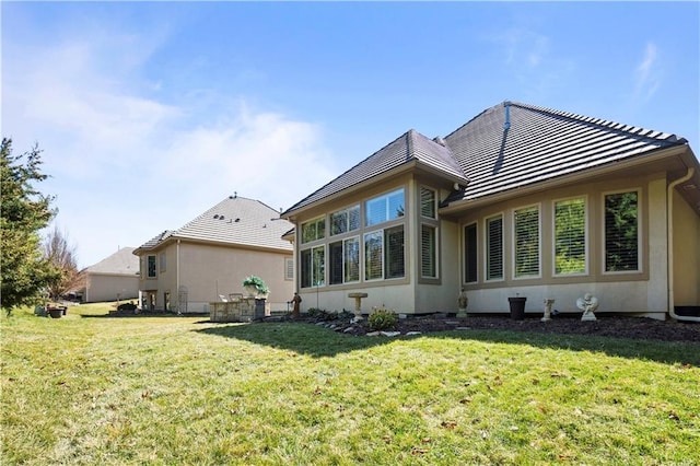 rear view of property with stucco siding, a lawn, and a tile roof