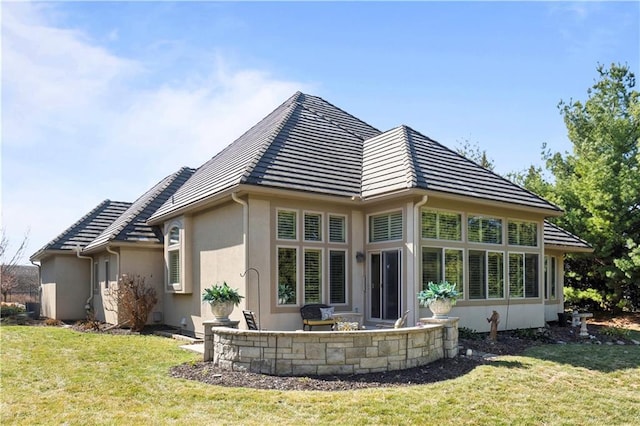 back of property featuring a tile roof, a lawn, and stucco siding