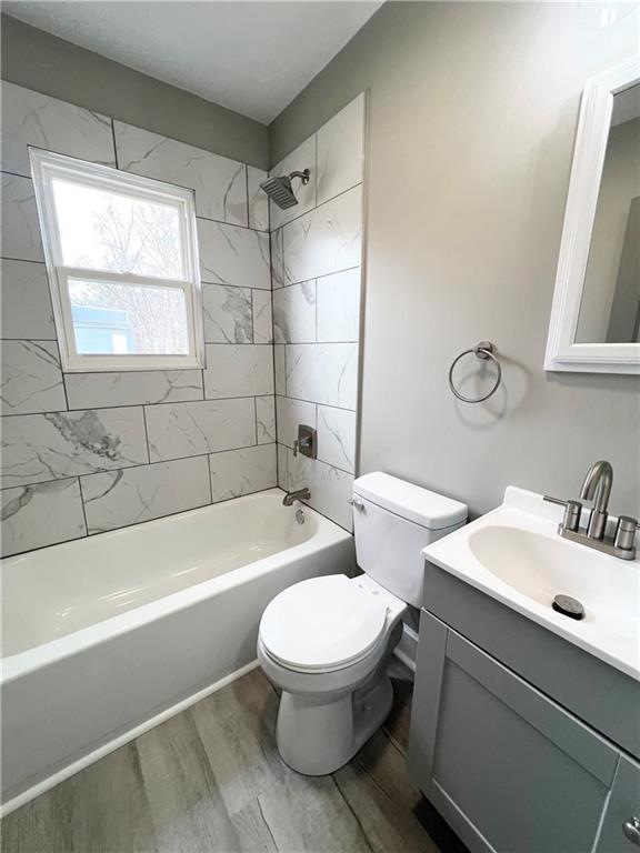 bathroom with washtub / shower combination, toilet, vanity, and wood finished floors