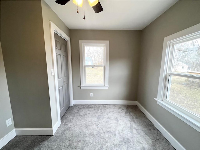 carpeted empty room featuring a ceiling fan and baseboards