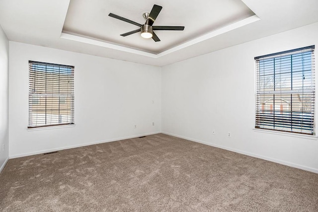 carpeted empty room with a raised ceiling, a healthy amount of sunlight, and ceiling fan