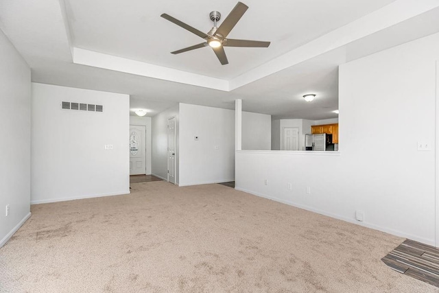 unfurnished living room with visible vents, carpet flooring, a raised ceiling, and baseboards