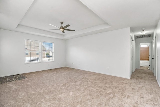 carpeted spare room featuring a tray ceiling, visible vents, baseboards, and ceiling fan