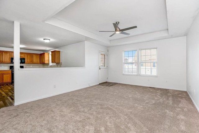 unfurnished living room with carpet flooring, ceiling fan, a raised ceiling, and baseboards