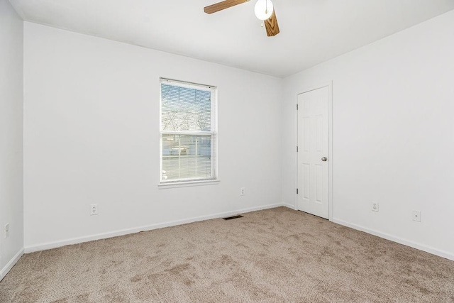 carpeted spare room with visible vents, baseboards, and a ceiling fan