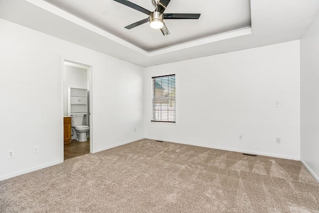 unfurnished bedroom featuring baseboards, a raised ceiling, connected bathroom, and carpet flooring