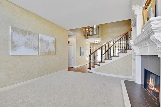 entrance foyer featuring baseboards, a tiled fireplace, stairway, carpet floors, and an inviting chandelier