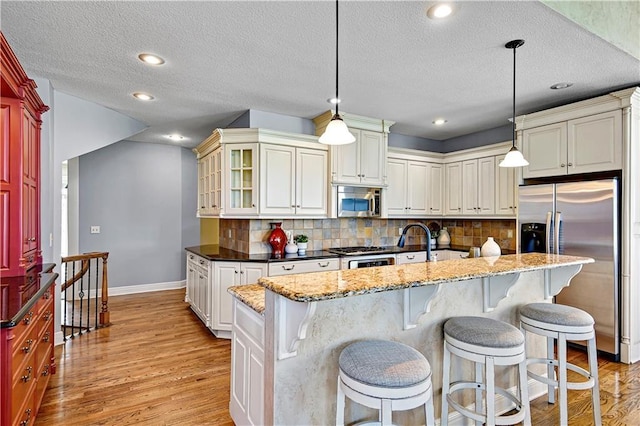 kitchen with light stone counters, light wood finished floors, appliances with stainless steel finishes, a kitchen breakfast bar, and backsplash