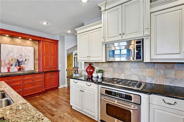 kitchen with dark stone countertops, light wood finished floors, appliances with stainless steel finishes, a textured ceiling, and tasteful backsplash