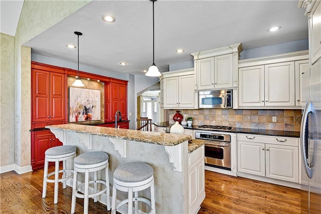 kitchen with tasteful backsplash, light stone countertops, decorative light fixtures, wood finished floors, and stainless steel appliances