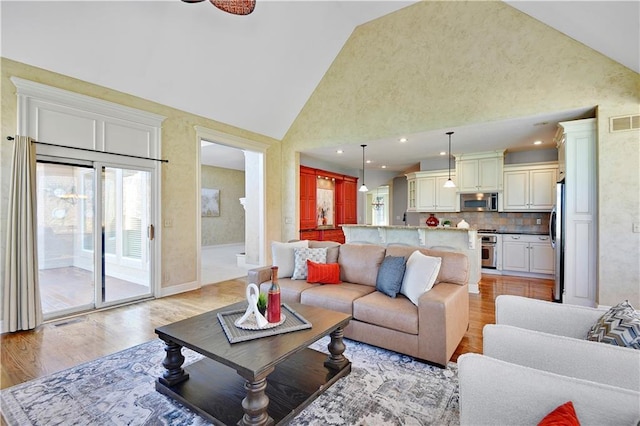 living area featuring visible vents, high vaulted ceiling, and light wood-style floors