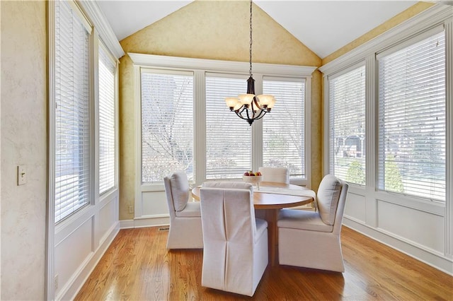 dining room featuring a notable chandelier, light wood-style floors, a decorative wall, a healthy amount of sunlight, and vaulted ceiling