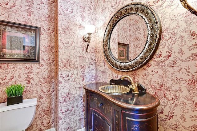 bathroom with toilet, vanity, and wallpapered walls