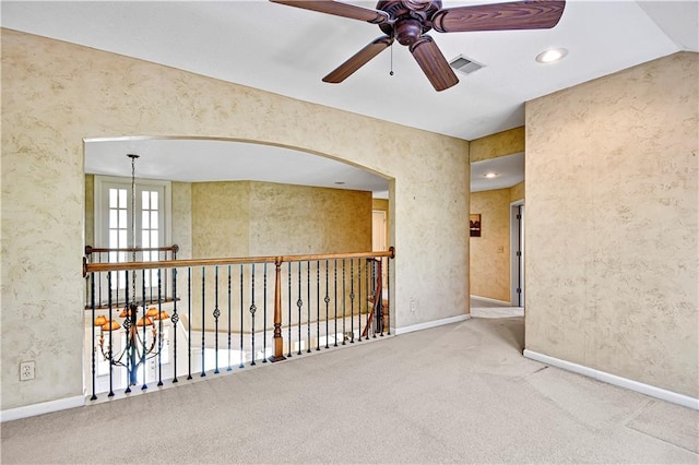 carpeted spare room featuring visible vents, wallpapered walls, baseboards, arched walkways, and a ceiling fan