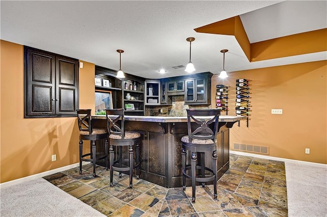 bar featuring baseboards, visible vents, hanging light fixtures, stone finish floor, and indoor bar