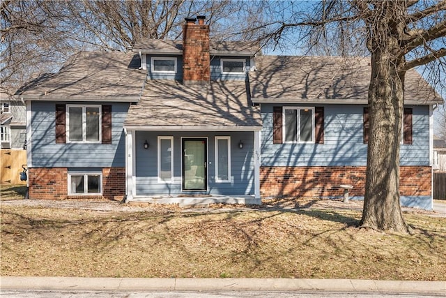 split level home with a front yard, roof with shingles, a porch, a chimney, and brick siding