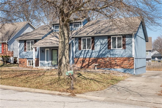 view of front of home featuring brick siding, a shingled roof, a front lawn, and fence