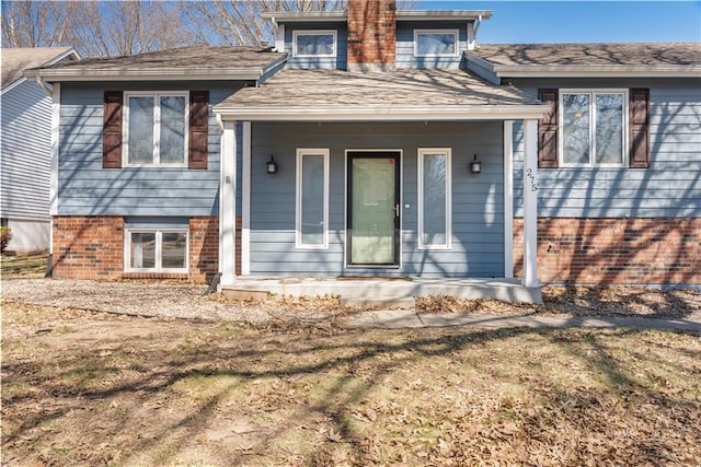 property entrance with brick siding, covered porch, and roof with shingles