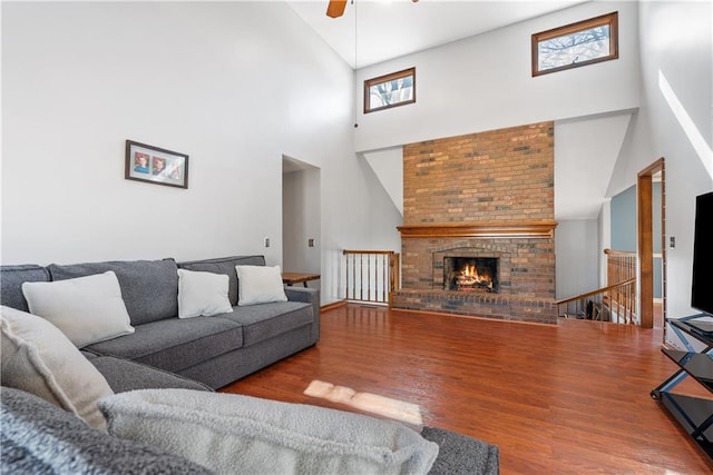 living area with a brick fireplace, ceiling fan, and wood finished floors