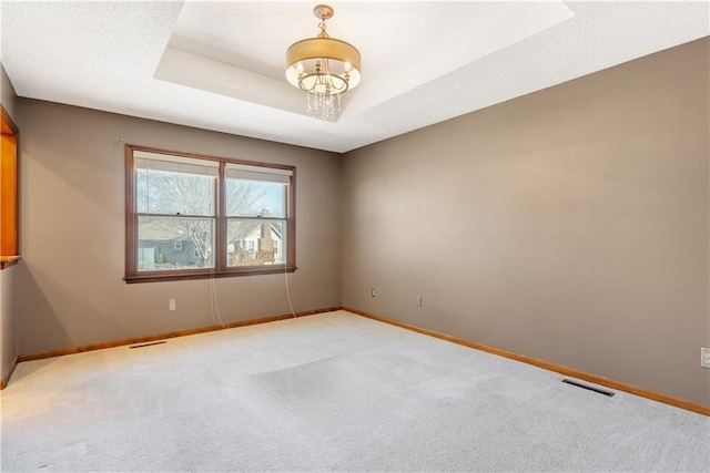 carpeted empty room featuring visible vents, baseboards, a textured ceiling, a raised ceiling, and a notable chandelier