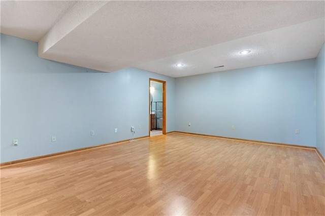 empty room featuring light wood-style flooring, baseboards, and a textured ceiling