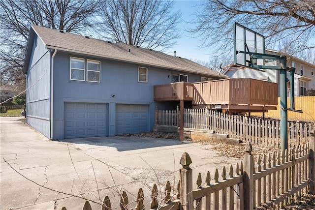 back of house featuring an attached garage, a shingled roof, driveway, and fence