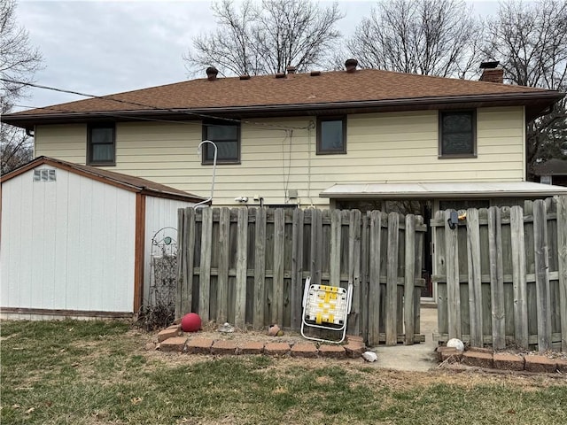 back of house with a shingled roof, fence, a chimney, an outdoor structure, and a storage unit