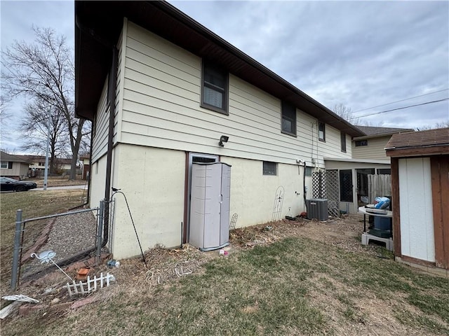 back of house with central air condition unit, a lawn, and fence