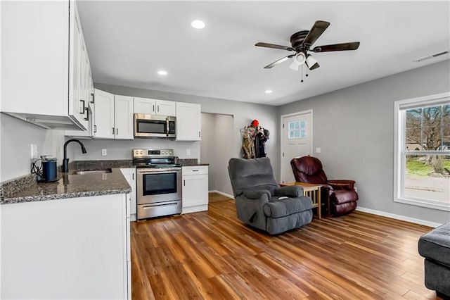 kitchen featuring open floor plan, wood finished floors, white cabinets, stainless steel appliances, and a sink