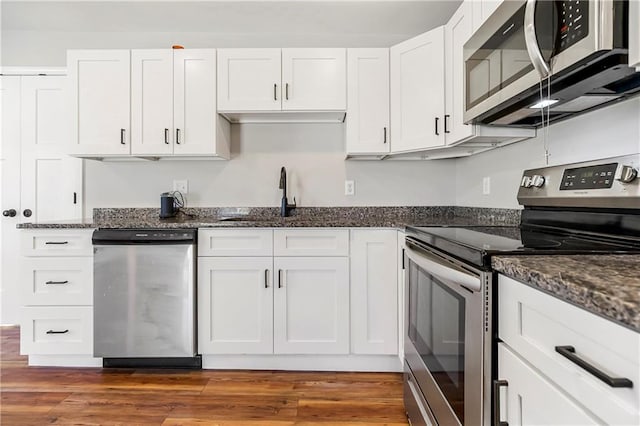 kitchen with dark stone countertops, white cabinets, wood finished floors, and stainless steel appliances