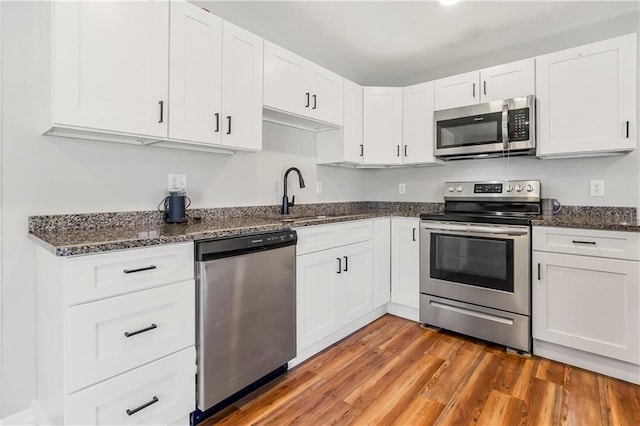 kitchen featuring dark stone countertops, stainless steel appliances, light wood-style floors, and a sink