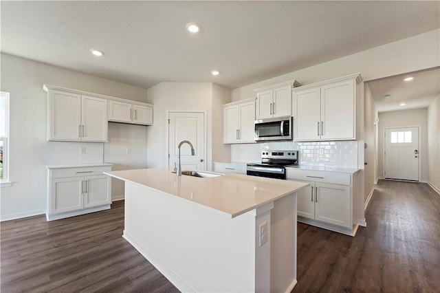 kitchen featuring a kitchen island with sink, decorative backsplash, appliances with stainless steel finishes, dark wood-style flooring, and a sink