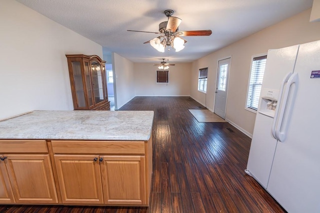 kitchen with baseboards, dark wood finished floors, a peninsula, ceiling fan, and white refrigerator with ice dispenser