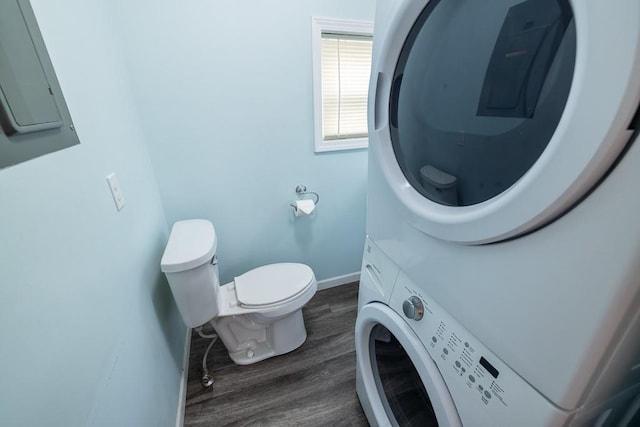 bathroom with toilet, electric panel, wood finished floors, stacked washer / drying machine, and baseboards